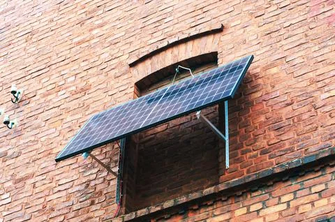 A solar panel is mounted on a brick wall, providing a source of renewable e.. Stock Photos