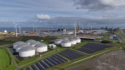 Solar panel park with windmills and fuel silos and harbor in background, Aerial Stock Footage 253802315
