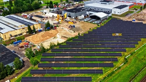 Solar Panel Rows on Grass Beside Industrial Buildings and Railway, Aerial Stockbeeldmateriaal 348899071