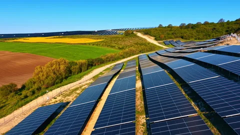 Solar panel rows on undulating terrain. Dark blue modules along a dirt path with Stock Footage 337064701