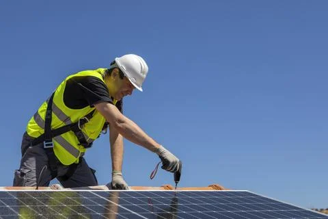 Solar panel technician with drill installing solar panels on roof 库存照片