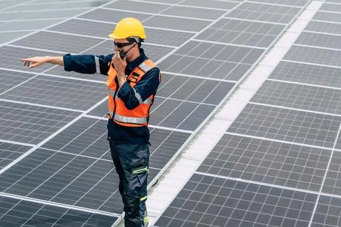 Solar panel technician inspecting a rooftop solar array while pointing at a.. Stock Photos