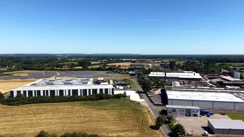 Solar-paneled warehouse roofs line rural road beside golden wheat fields in Stock Footage 342219991