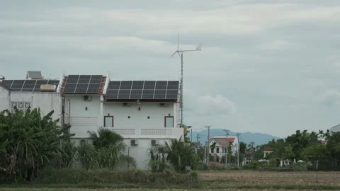 Solar panels and a small wind turbine operating on a modern house surrounded by Stock Footage 344718653