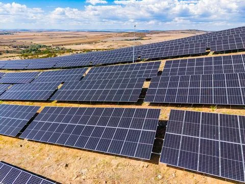 Solar panels are arranged in rows on a hillside under a blue sky with cloud.. Fotos Stock