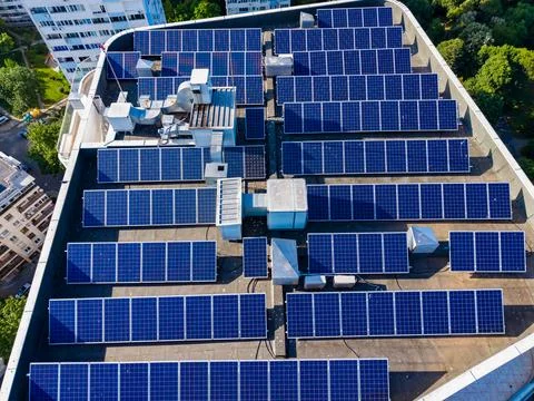 Solar panels are installed on a flat rooftop in an urban setting. Many panels Stock Photos