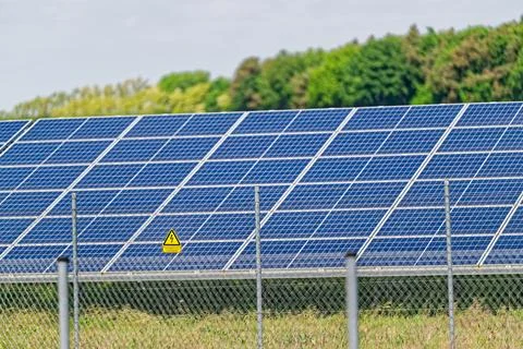 Solar panels array in a green field with safety fence and warning sign 写真素材