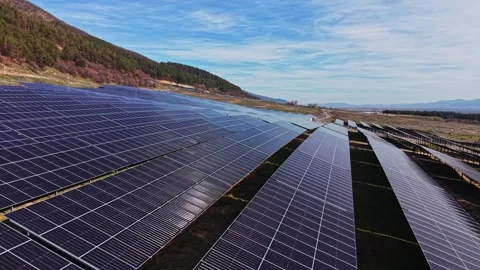 Solar panels cover fields under blue sky with mountains in background Stockbeeldmateriaal 334033191