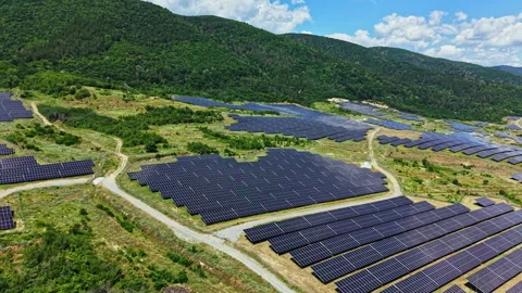 Solar panels cover a large area on land near hills with blue sky and clouds Stock Footage 340884189