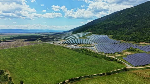 Solar panels cover a large area on a hillside with green fields in the Stock Footage 341132600