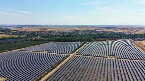 Solar panels cover large fields near a town with wind turbines in the distance Stock Footage 342746174