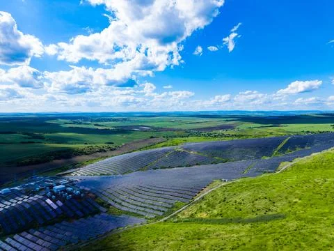 Solar panels cover large fields under a blue sky with clouds in an open lan.. Stock Photos