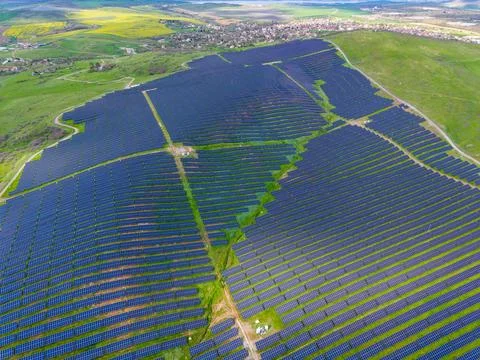 Solar panels cover a large flat area with green grass. The landscape shows ro Stock Photos