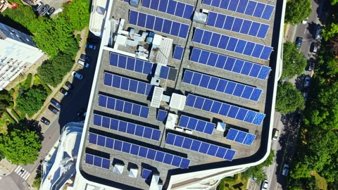 Solar panels cover a large rooftop in an urban area with cars parked below and Stock Footage 339495910
