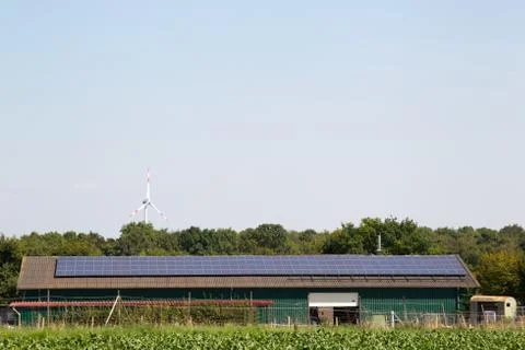 Solar panels on farming building with wind turbine in background Stock Photos