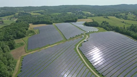 Solar panels installed on uneven meadow terrain surrounded by forest Stock Footage 314376554