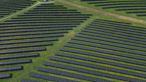 Solar panels installed on uneven meadow terrain surrounded by forest Stock Footage 314376555
