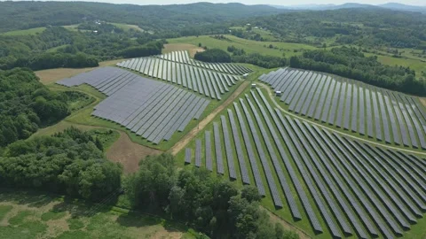 Solar panels installed on uneven meadow terrain surrounded by forest Stock Footage 314376657