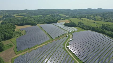 Solar panels installed on uneven meadow terrain surrounded by forest Stock Footage 314376684