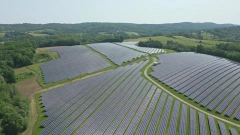 Solar panels installed on uneven meadow terrain surrounded by forest Stock Footage 314376685