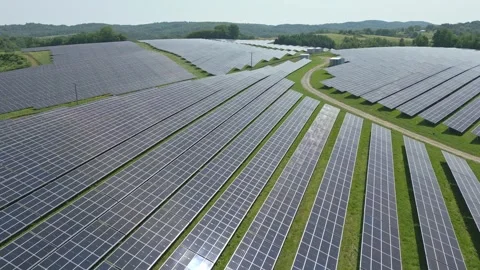 Solar panels installed on uneven meadow terrain surrounded by forest Stock Footage 314377174
