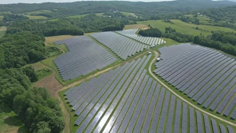 Solar panels installed on uneven meadow terrain surrounded by forest Stock Footage 314377186