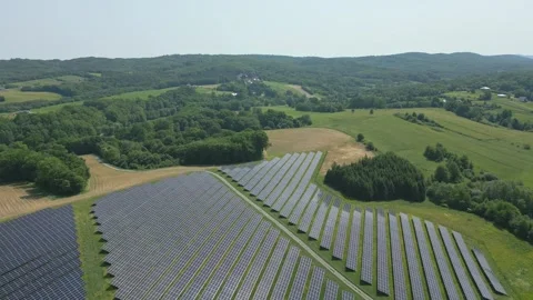 Solar panels installed on uneven meadow terrain surrounded by forest Stock Footage 314377234