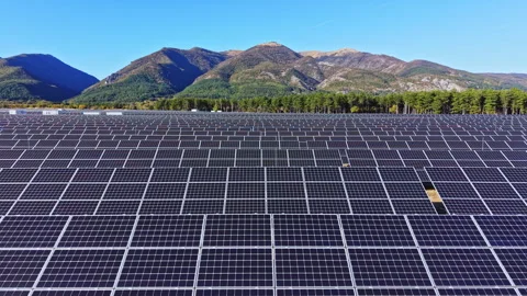 Solar panels in a large field with mountains in the background during a sunny Stock Footage 347756571