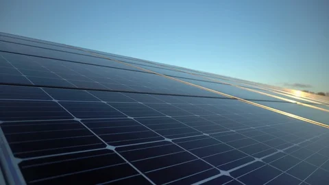 Solar panels reflecting sun in solar farm field at sunset, camera pan Stock Footage 128945247