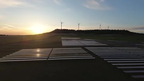 Solar Panels Reflecting Sunset Light with Wind Turbines in Background Stock Footage 330051276