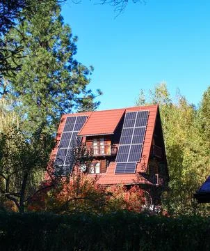 Solar panels on a rustic cabin surrounded by green trees on a bright autumn day Stock Photos