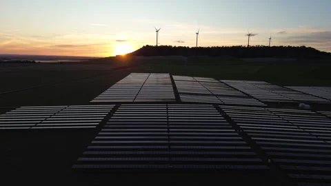 Solar Panels at Sunset Producing Renewable Energy with Wind Turbines on Horizon Stock Footage 330945609