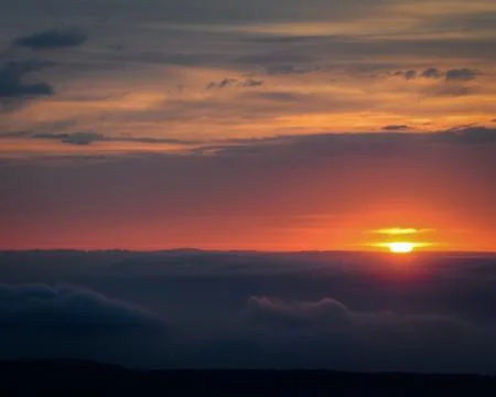 The Solar Sphere descends between High Clouds and Low Fogs Stock Photos