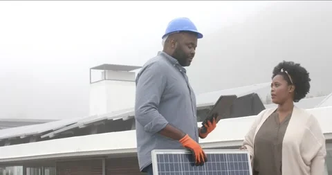 Solar tech with helmet reading tablet guiding woman checking panel and plug Stock Footage 342363129