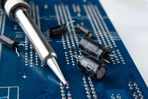Soldering iron on the background of a computer Board and capacitors in soft f Stock Photos