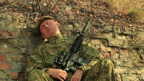 Soldier with automatic rifle  sleep and wake up near  brick wall  Stock Footage 69787282