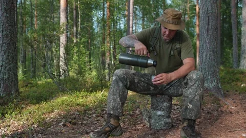 A soldier on a break in the forest pours himself tea from a thermos. Military Stockbeeldmateriaal 314446126