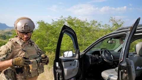 Soldier in full combat gear is saying something. Stands near the open car door Stock Footage 129456574