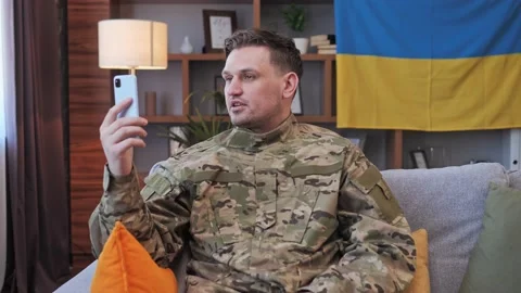 Soldier having Video call using mobile phone Ukrainian flag on the background. Video stock 172397467