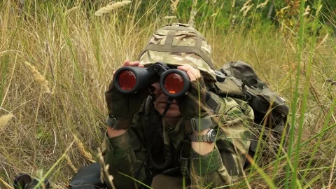 Soldier looking through binoculars while sitting in ambush Stock Footage 166361265