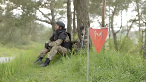 Soldier with mine detector and backpack sits exhausted by a tree after demining Stock-Footage 244926068