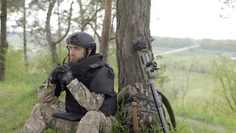 Soldier with mine detector and backpack sits exhausted by a tree after demining Video stock 244926367