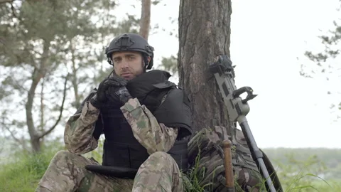 Soldier with mine detector and backpack sits exhausted by a tree Video stock 255058834