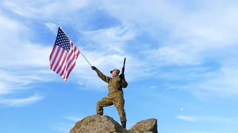   Soldier on mountain top with automatic rifle,  and  American Flag. Slow Motion Stock Footage 70078175