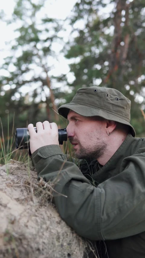 Soldier observing enemy through binoculars while hiding in forest position. Stock Footage 326761680