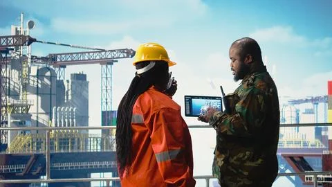 Soldier on offshore platform deck talking with technician, using device 스톡 사진