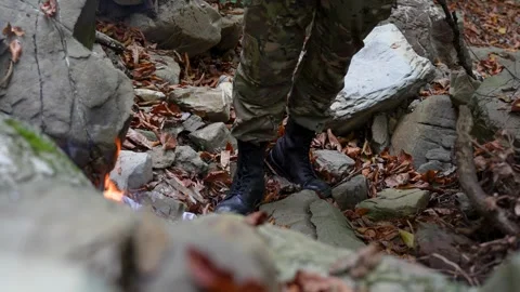 Soldier or Survivalist setting a fire in a rocky, wooded area Stock Footage 320422258