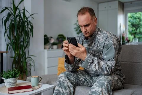 Soldier sitting on sofa using smartphone at home Stock Photos