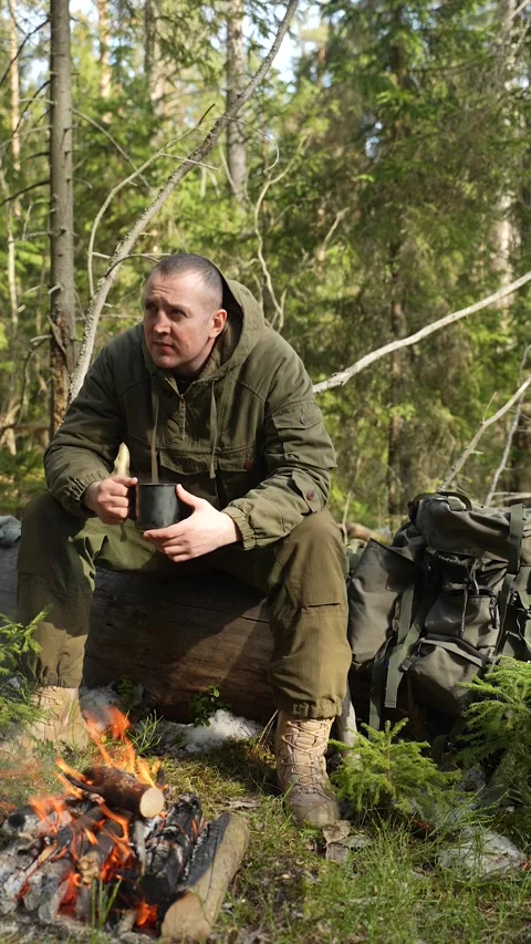 A soldier in tactical gear drinks tea by a campfire in the forest. A ranger Video stock 307004606