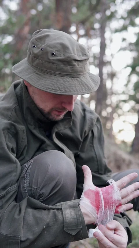 Soldier treating a hand wound during combat in forest terrain. Stock Footage 326761683
